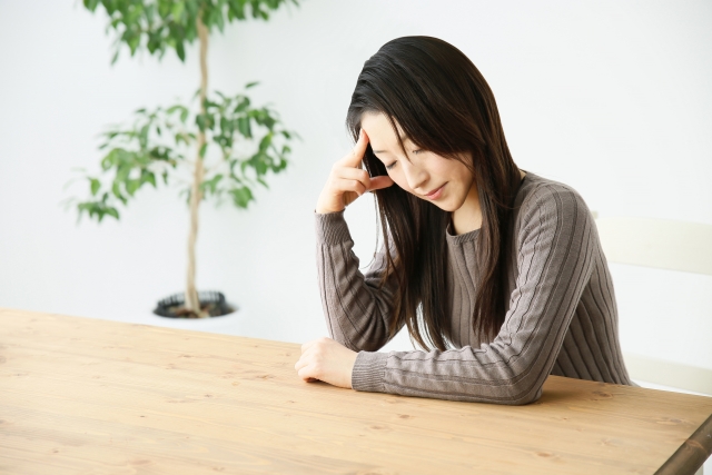 テーブルに肘をつき頭痛にうなだれる女性