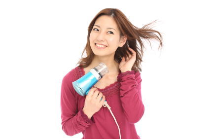 下から髪の根元にドライヤーの温風を当てる女性